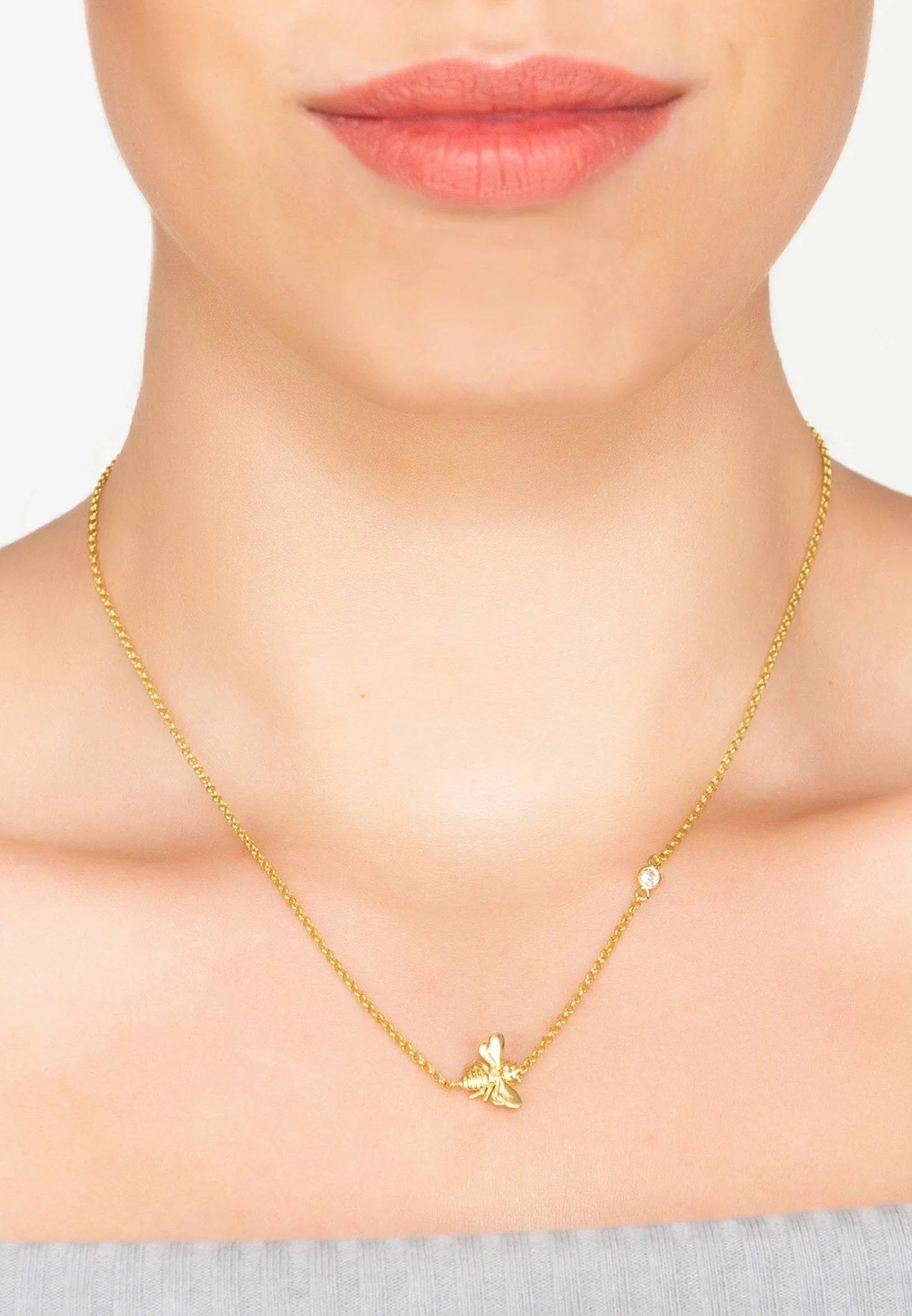 Eine Person trägt eine goldene Halskette mit einem kleinen Schmetterlingsanhänger und einem einzelnen runden Edelstein, gestylt auf nackter Haut und einem grauen schulterfreien Oberteil - ein eleganter Look ähnlich der LATELITA Halskette "Kunigunde", vergoldet.
