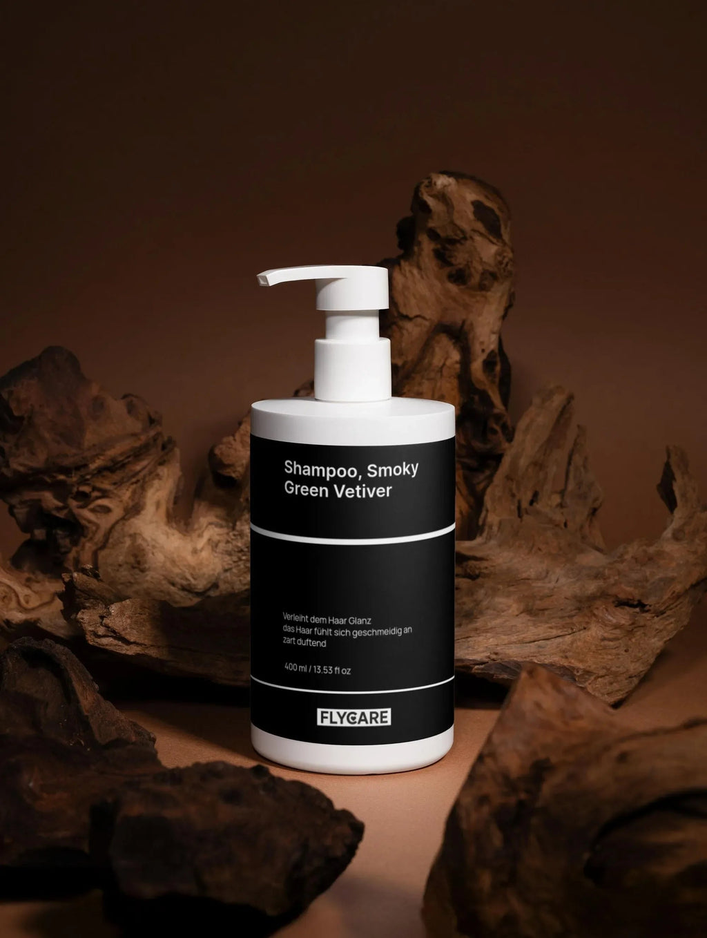 Shampoo Smoky Green Vetiver von Flycare, in weißer Flasche mit schwarzem Etikett vor braunem Hintergrund und Holzwurzeln.
