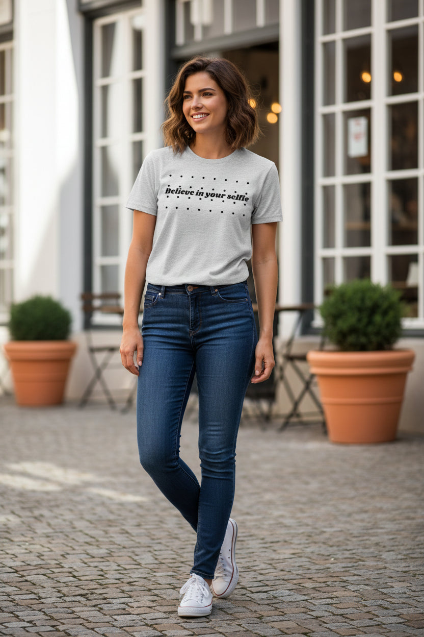 Grey cotton T-shirt by flyliving, featuring "Believe in your selfie" text and black dots, worn by a woman outdoors.