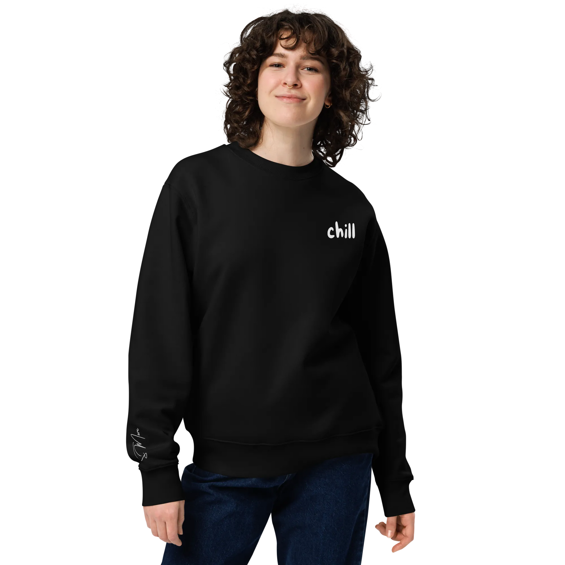 Eine Person mit lockigem Haar lächelt, sie trägt den schwarzen flyliving Pullover "chill" aus 100% organischer Baumwolle und eine blaue Jeans, vor einem schlichten Hintergrund - ideal für einen entspannten Lifestyle.